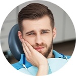 Man in pain holding his cheek in dental chair