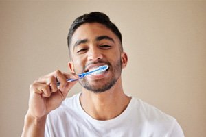 Man in white shirt smiling while brushing his teeth