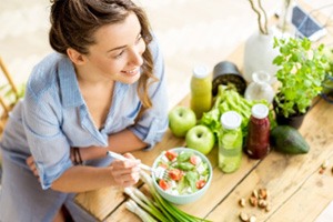 Woman eating salad on table with fresh juices, fruits, and herbs