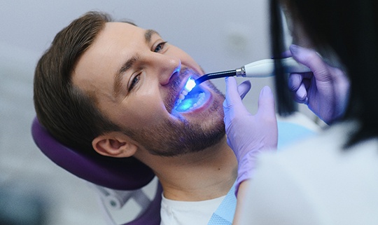 Dentist applying UV light to man’s filling