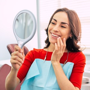 A woman admiring her dental implants in a hand mirror