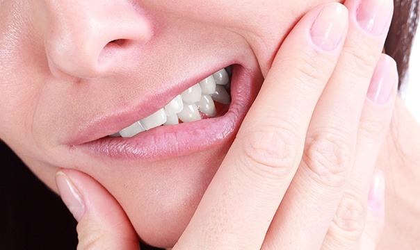 Woman in need of root canal therapy holding cheek in pain