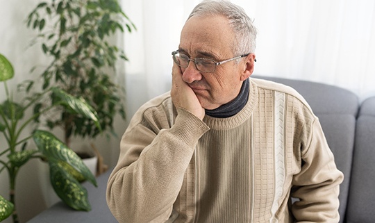 Senior man rubbing jaw due to discomfort