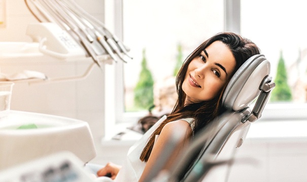 Woman smiling in dental chair after treatment for tooth sensitivity