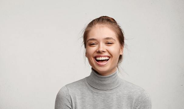 Woman in gray turtleneck sweater laughing after porcelain veneer placement