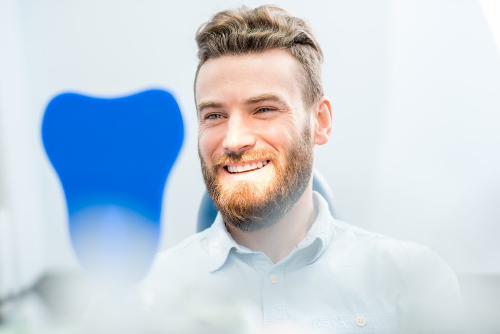 Man with beard smiling while looking in dentist's mirror