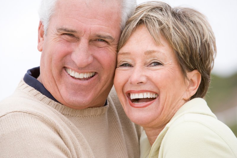Elderly couple leaning on each other and smiling with white teeth