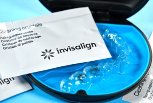 Zoom in of an aligner tray in its container with a packet of Invisalign cleaning crystals resting on top