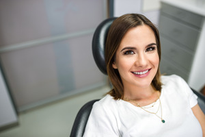 Woman in white shirt sitting in dental chair and smiling